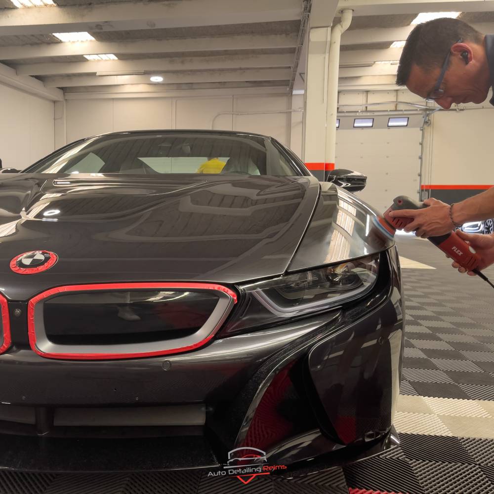 Detailer polissant à la machine le capot d'une BMW i8 noire dans l'atelier