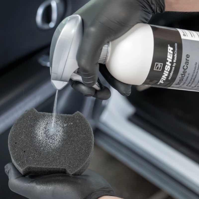 Application du dressing Koch-Chemie InsideCare pulvérisé sur une éponge, mains gantées dans un habitacle de voiture